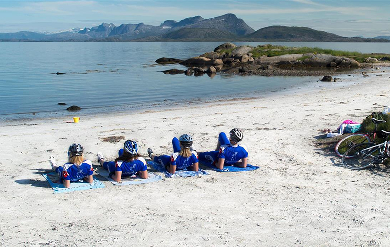 Bilde av 4 syklister som har tatt pause på en strand