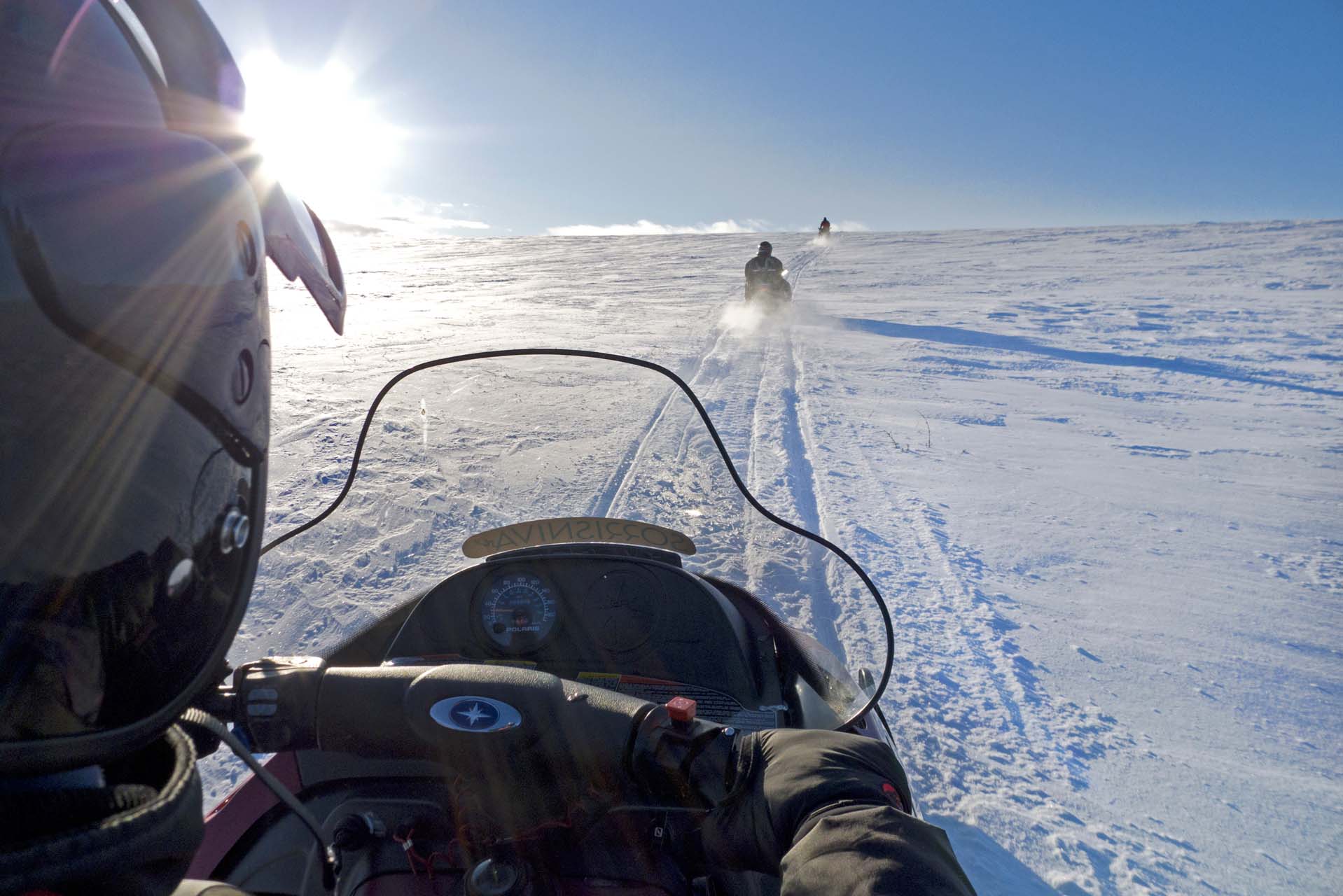 3 personer på snøscooter i sola